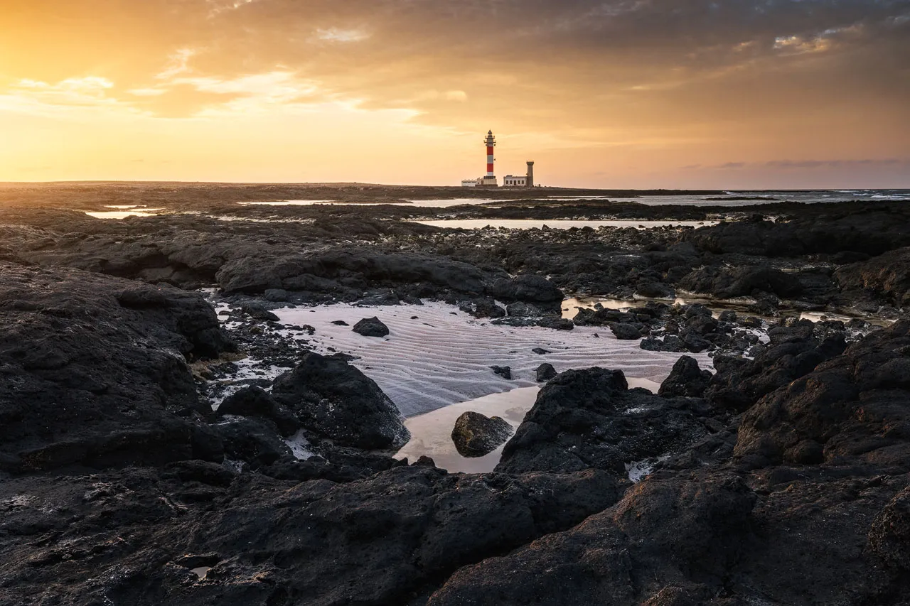 Golden light at Faro de Toston with dark rocks in foreground