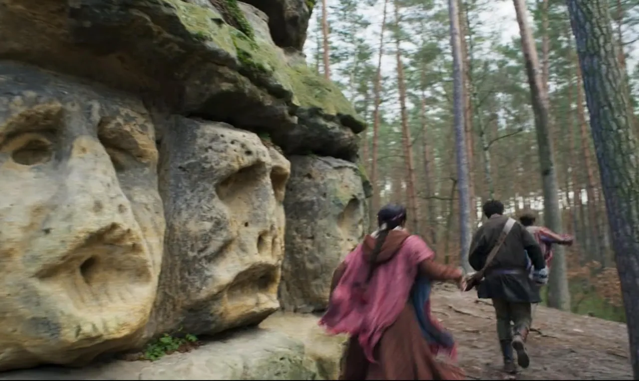 Screenshot of three people running near a worn-out ancient monument carven into the stone of the cliff face