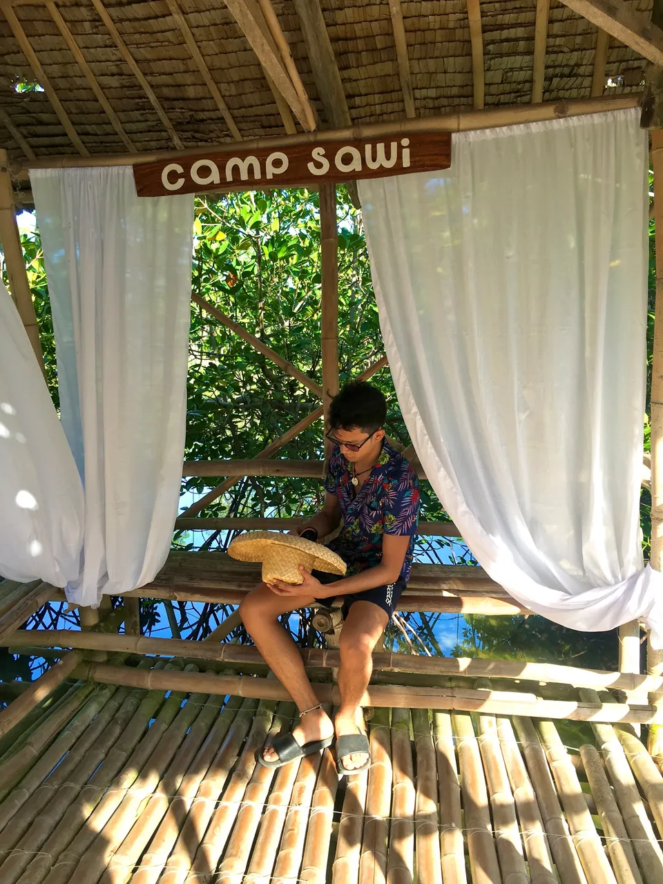 Small huts are stationed intermittently along the bamboo walkways, offering shade and respite. You can notice the wooden banner "Camp Sawi" where shots from the movie took place