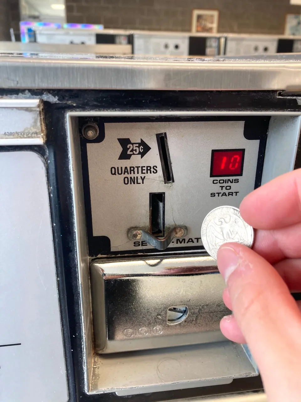 Public domain stock photo -- closeup of a hand inserting quarter's into a pay washing machine at a laundromat
