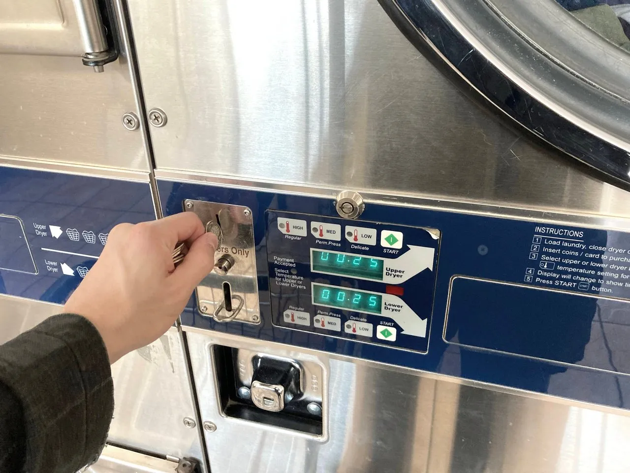 Public domain stock photo of a person's arm putting quarter's into a dryer machine at a laundromat