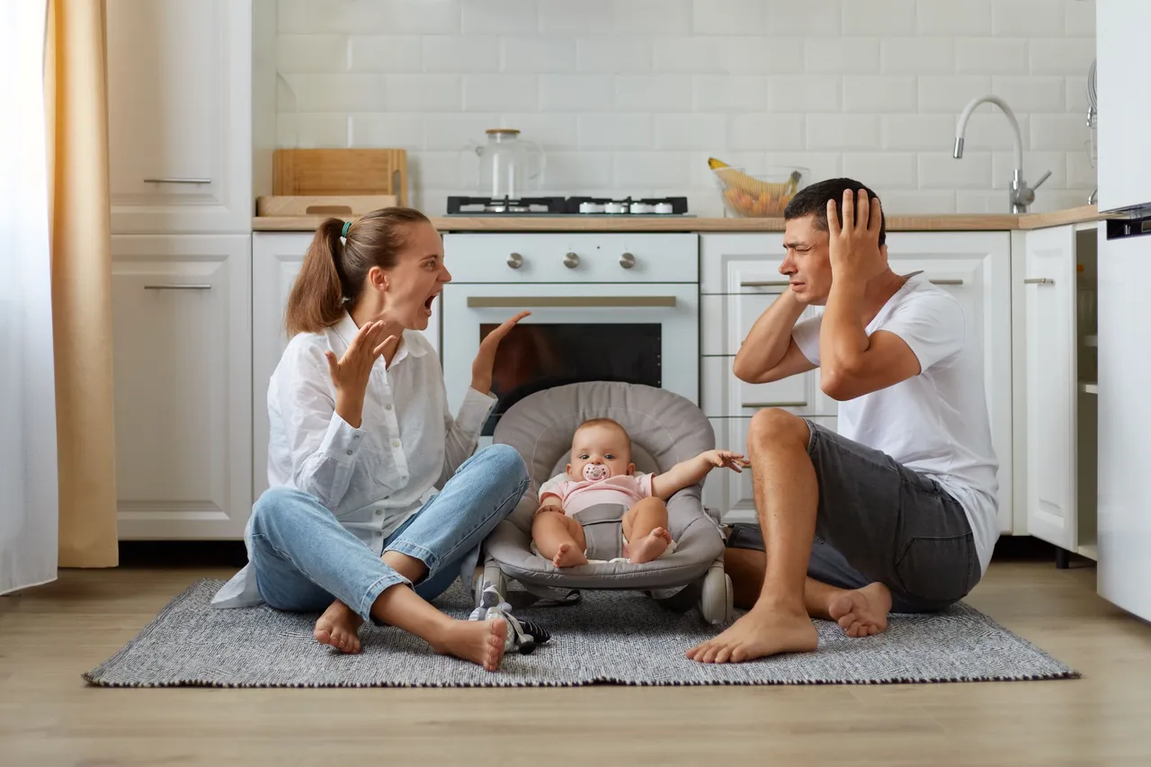 indoor-short-of-arguing-couple-sitting-on-the-floor-in-kitchen-wife-screaming-loudly-husband-covering-ears-with-palms-family-posing-with-infant-baby-in-rocking-chair.jpg