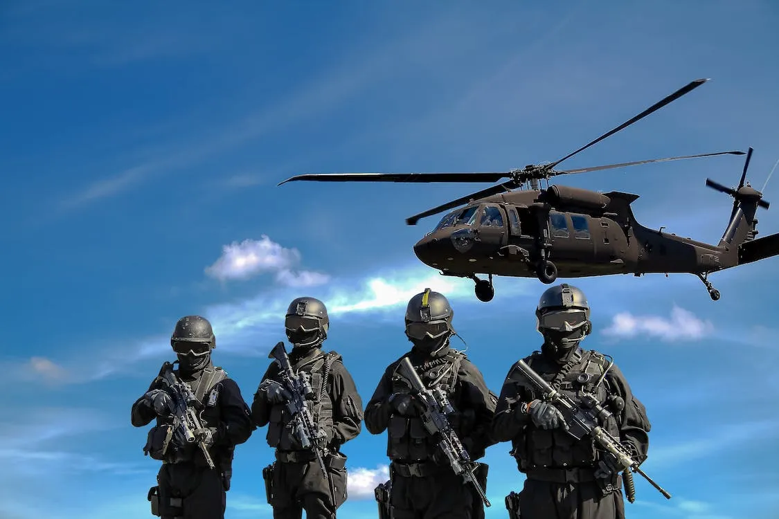 "Four Soldiers Carrying Rifles Near Helicopter Under Blue Sky"