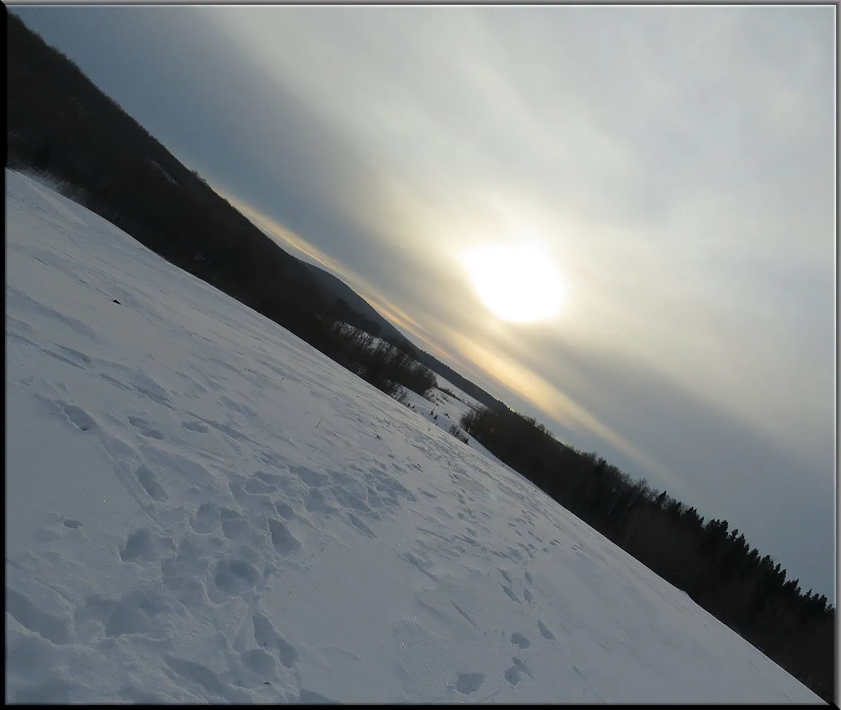 clouded sun sitting low in sky snowy trail leads to lake.JPG