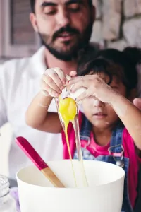 Father and daughter baking together. Daughter is cracking an egg into a bowl