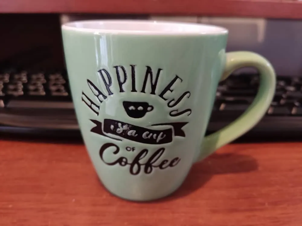 Foto de taza de café encima de una mesa de compuadora con el teclado en el fondo