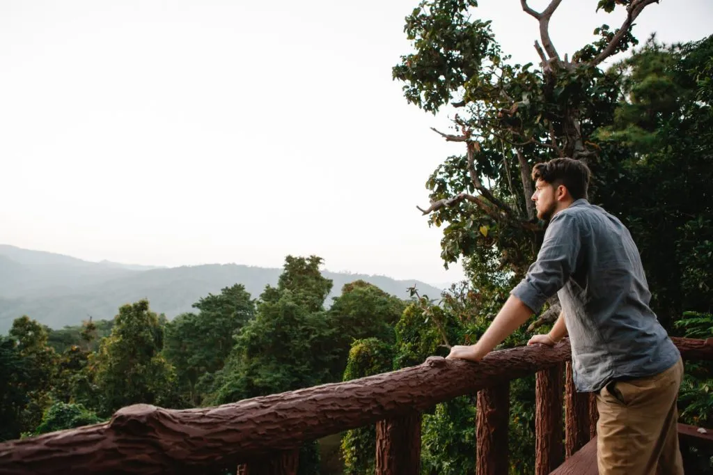 pensive young guy enjoying mountain view from wooden terrace