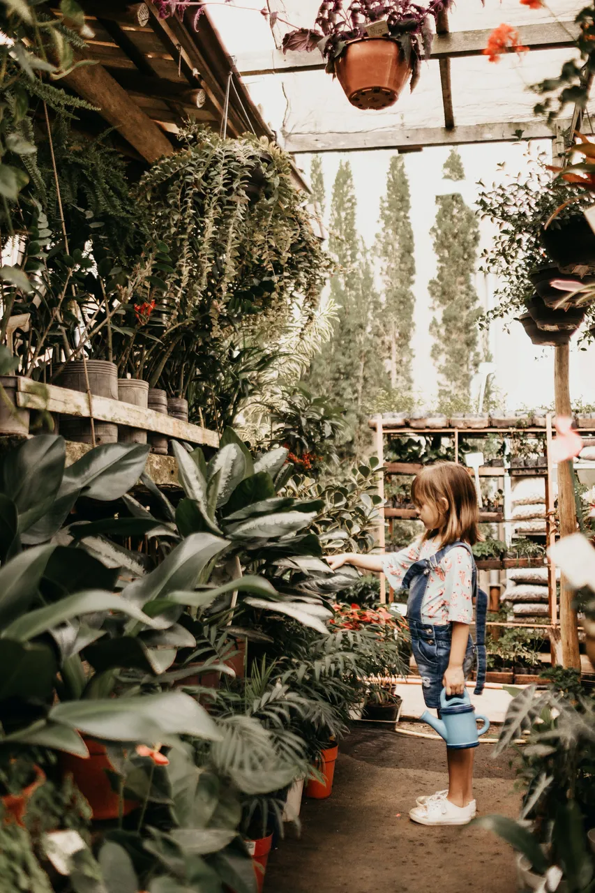 girl holding teal watering can surrounded by plant