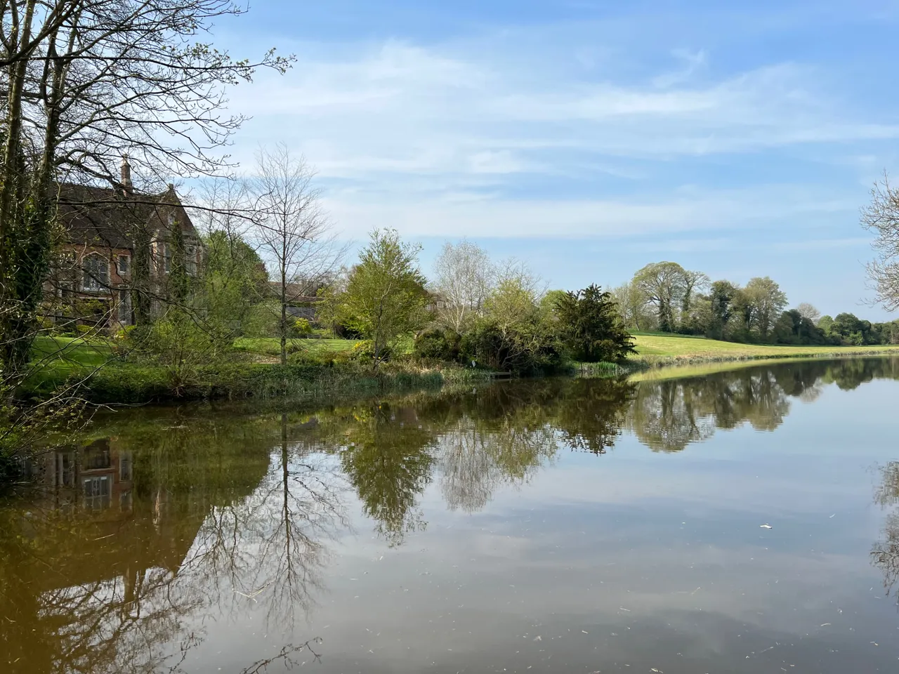 Edge of village opens out into a wide stretch of water, wooded copse and pasture