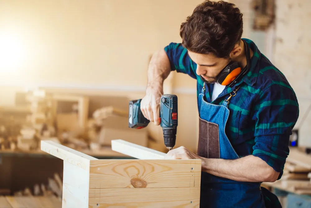 Carpenter drills a hole with an electrical drill.png