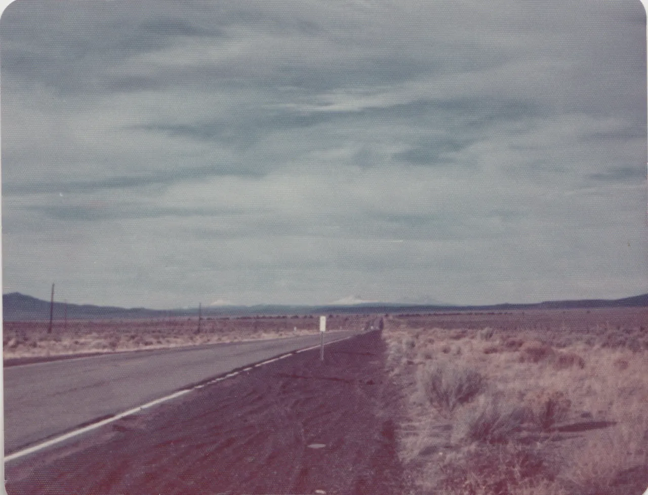 1974-11-24 - Sunday - Burns to Bend, a road in the wilderness, plains, blue mountains, cloudy sky, flat brush land, 1pic.png
