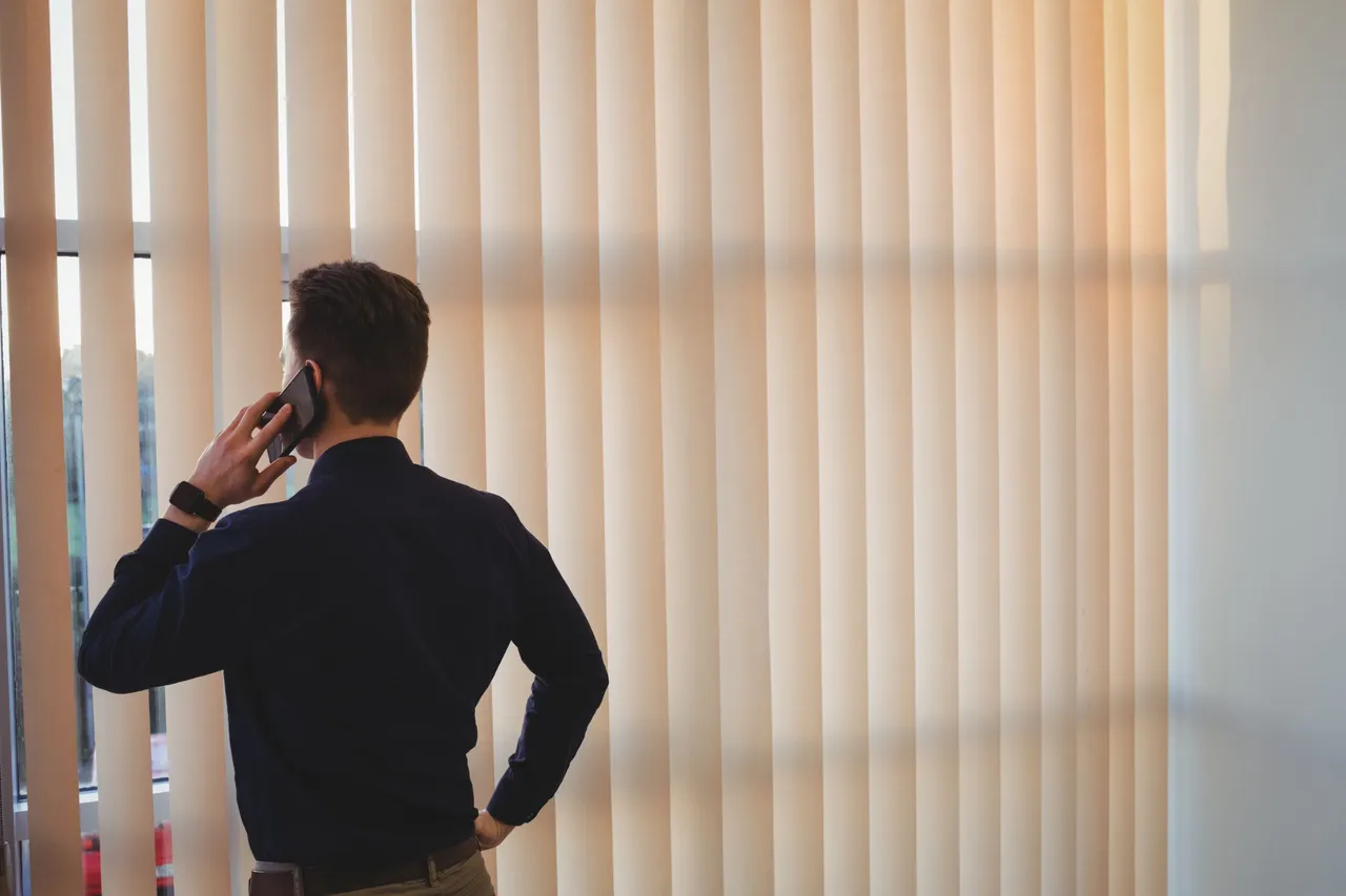 male-executive-talking-mobile-phone-near-window-blinds.jpg
