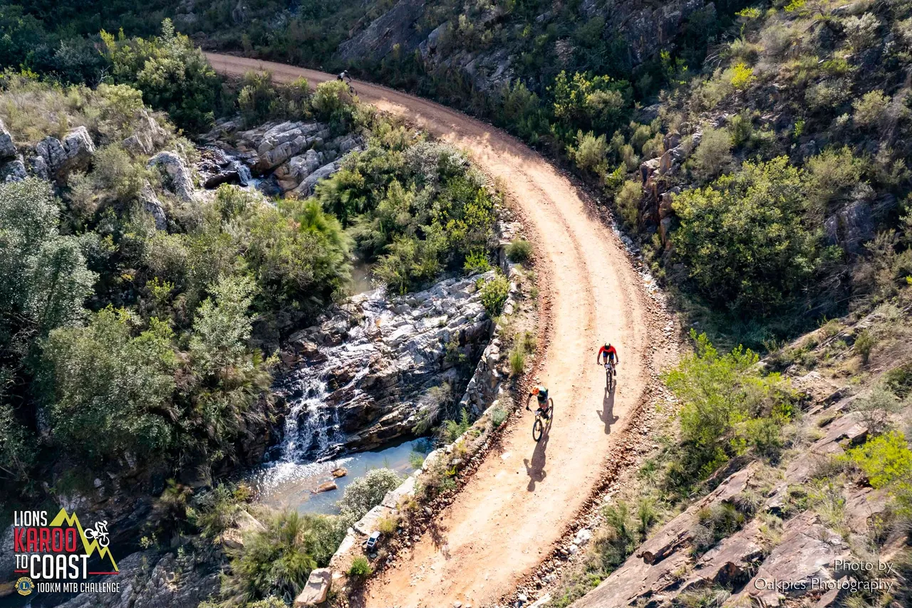 May be an image of 2 people, road and text that says 'LIONS KAROO KARDO の光 TOCOAST 100KM 100KMTBCHALLERCE KИMTB CHALLENGE Photoby Oakpies Phatogr @akpiesPhategraphy aphy'