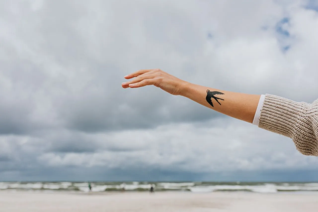 kaboompics_A woman's hands with a swallow tattoo raised to the sky.jpg