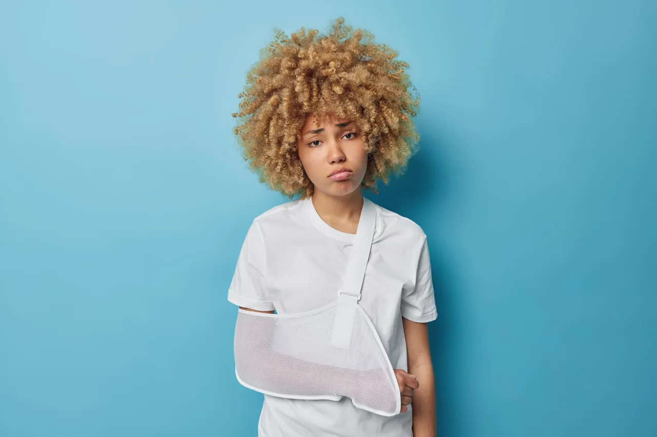 curly-haired-upset-european-woman-has-problems-with-health-injured-broken-arm-looks-sadly-camera-dressed-casual-t-shirt-isolated-blue-background-female-patient-comes-surgeon.jpg