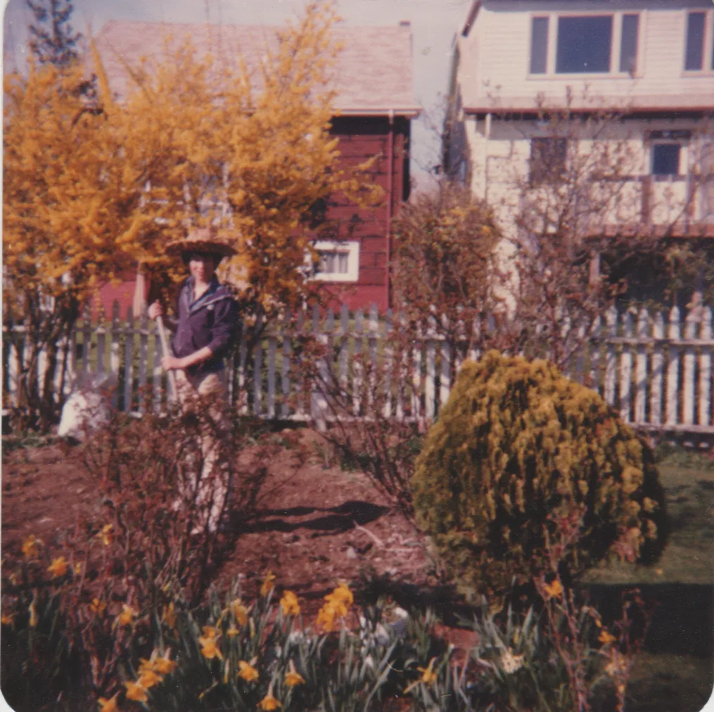 1980 - Spring - Mike - Grandma's Yard. flowers, holding a shovel or something, garden, outside, hat.png
