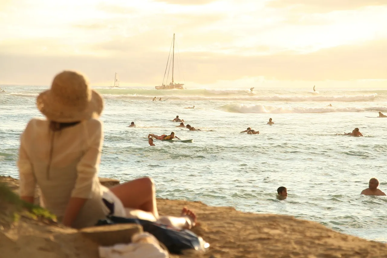 A person sits on the beach watching other people surf.