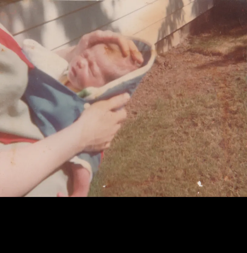1980-07-05 - Saturday - Katie Arnold at 12 days old, mom is holding her in blue thing, on grass, by house.png