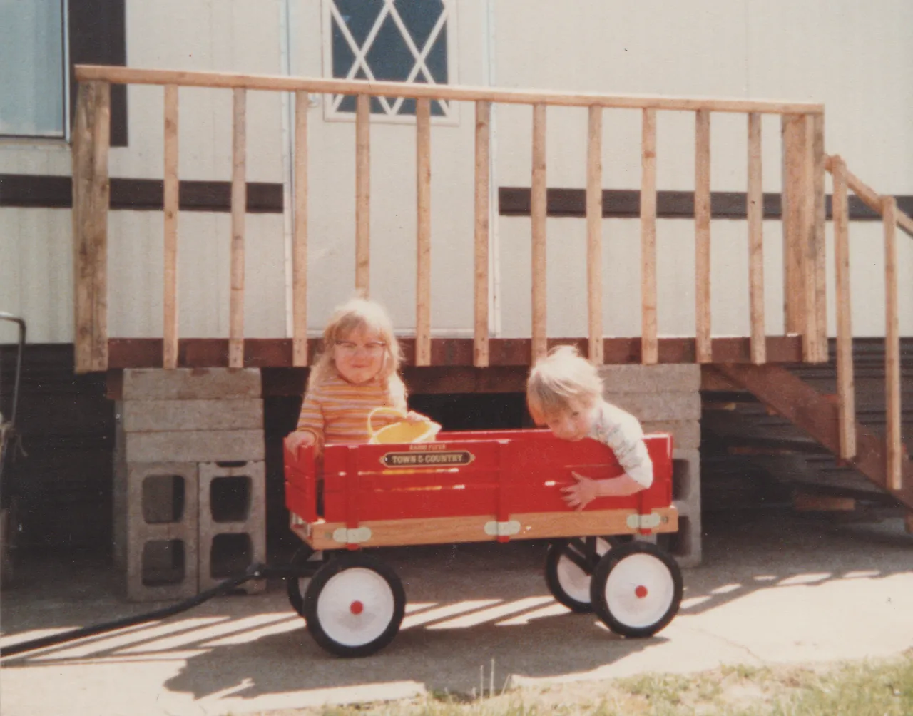 1984 - Early - Katie & long-hair Ricky in the red wagon by the front porch.png